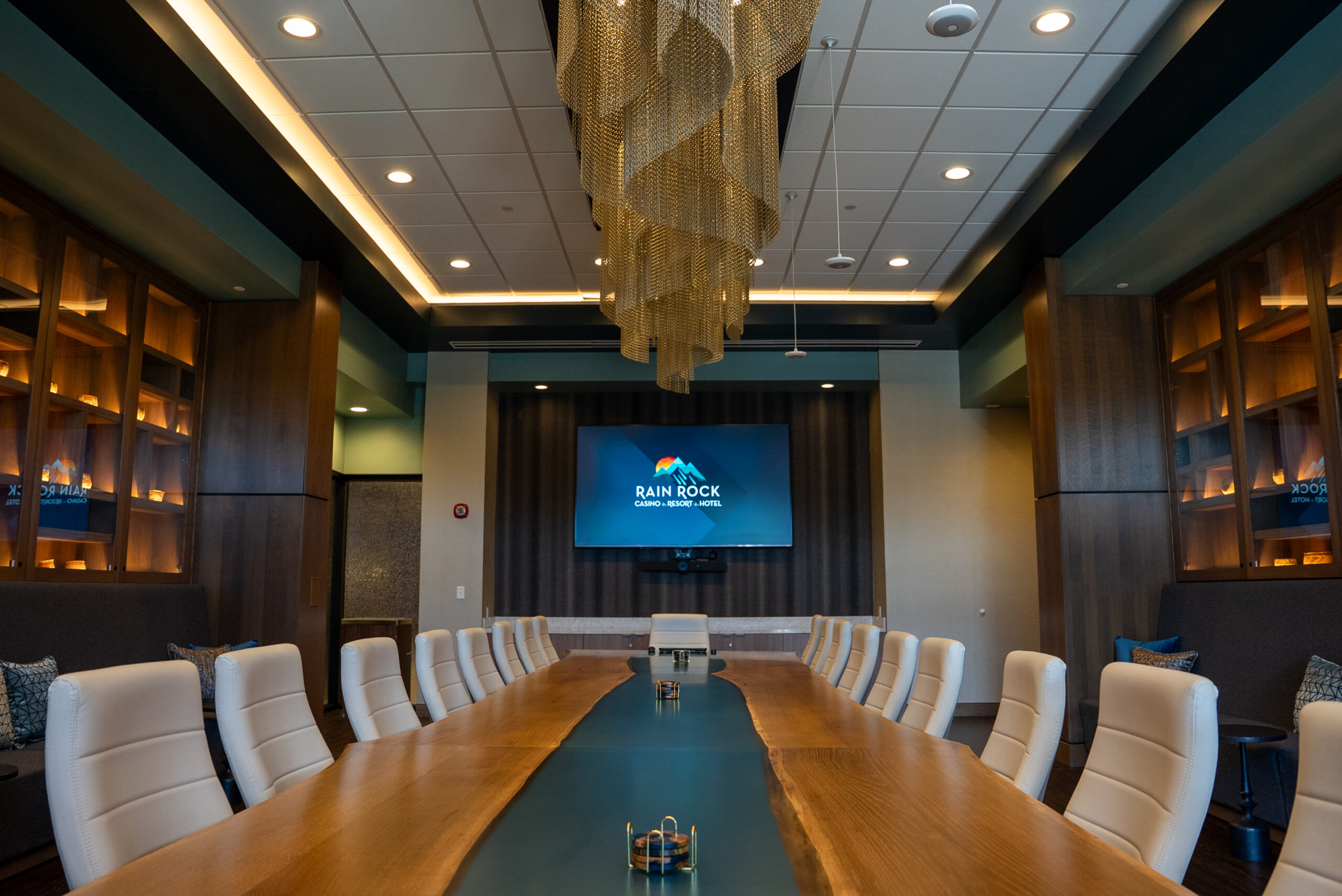 Modern conference room with long boardroom table, white chairs, and large display screen